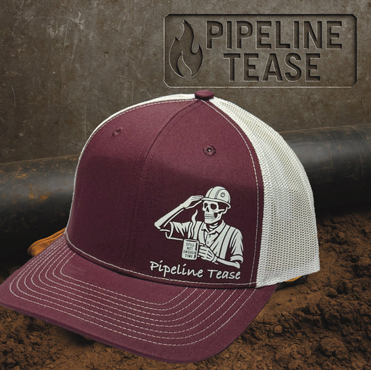 Maroon and white trucker hat featuring the Pipeline Tease white Still Not Enough Time logo holding a coffee cup, displayed on a dirt jobsite background with Pipeline Tease branding.