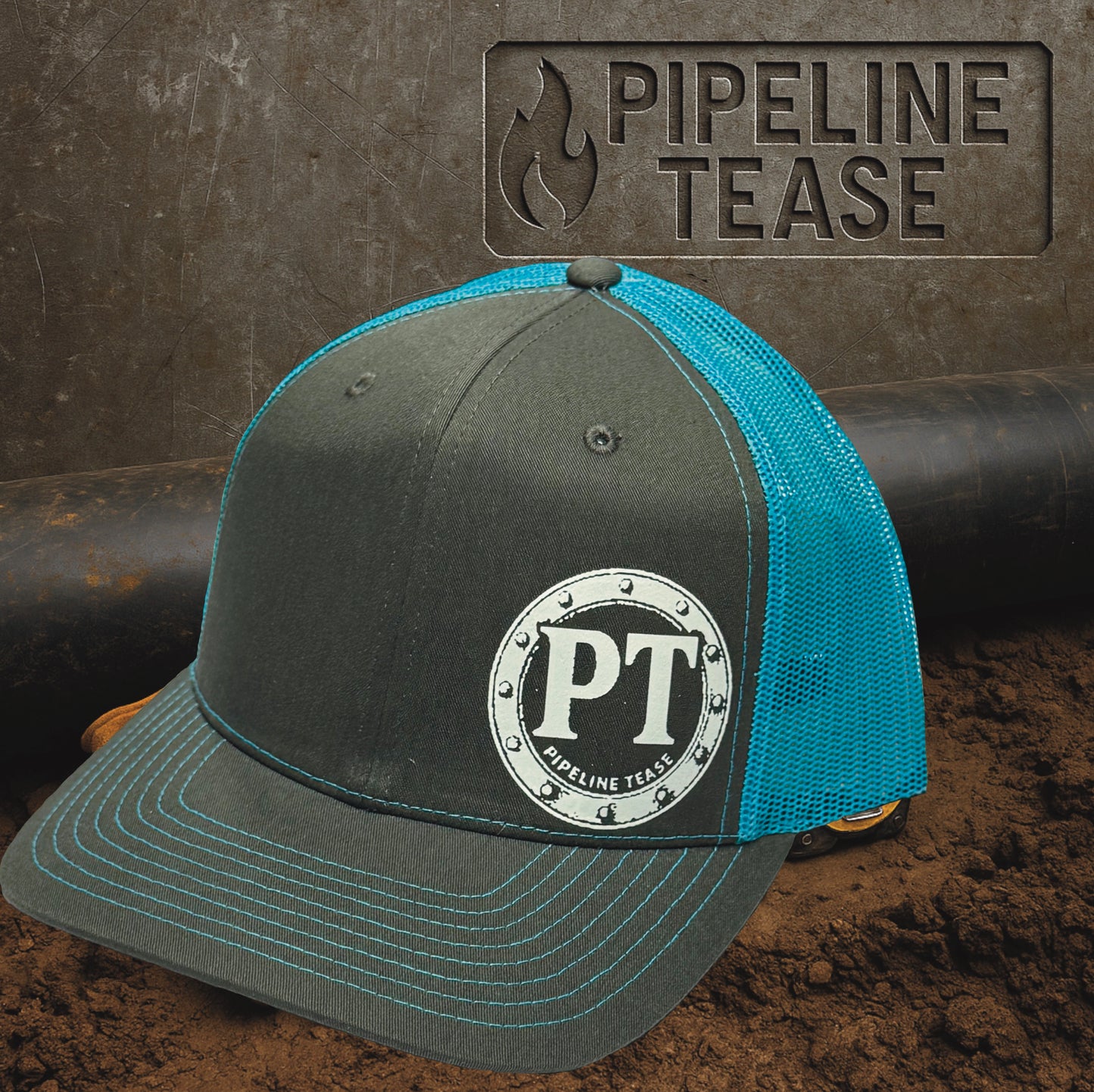 Dark grey and teal trucker hat featuring the Pipeline Tease white PT Flange logo, displayed on a dirt jobsite background with Pipeline Tease branding.