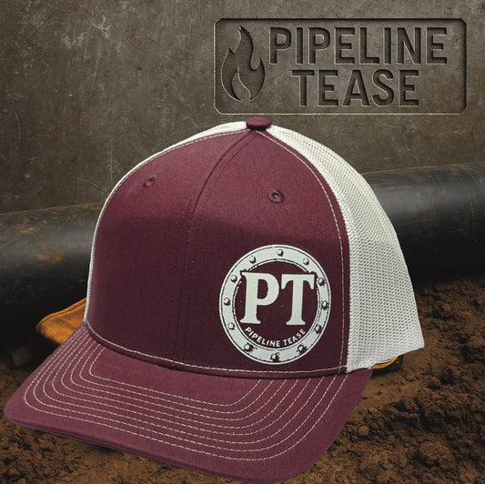 Maroon and white trucker hat featuring the Pipeline Tease white PT Flange logo, displayed on a dirt jobsite background with Pipeline Tease branding.